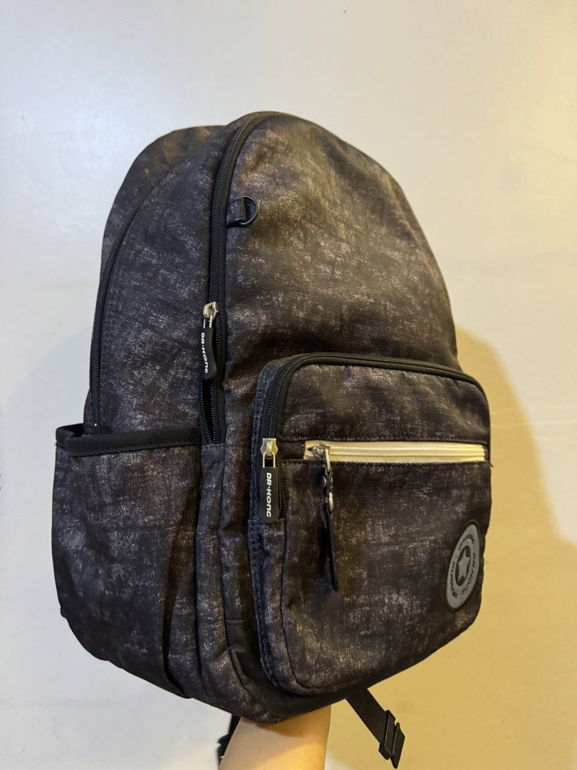Dr. Kong grey textured school backpack with multiple compartments (Category: Backpacks) located in Urdaneta. Submitted by kathleenja24136 (Listing ID 1465472633, Image 2). Description: - Brand: Dr. Kong - Color: Grey textured fabric with contrasting white front zip - Compartments: Multiple zipped compartments and convenient side mesh pockets for water bottles - Comfort & Safety: Padded mesh shoulder straps with reflective strips and a sturdy rubb