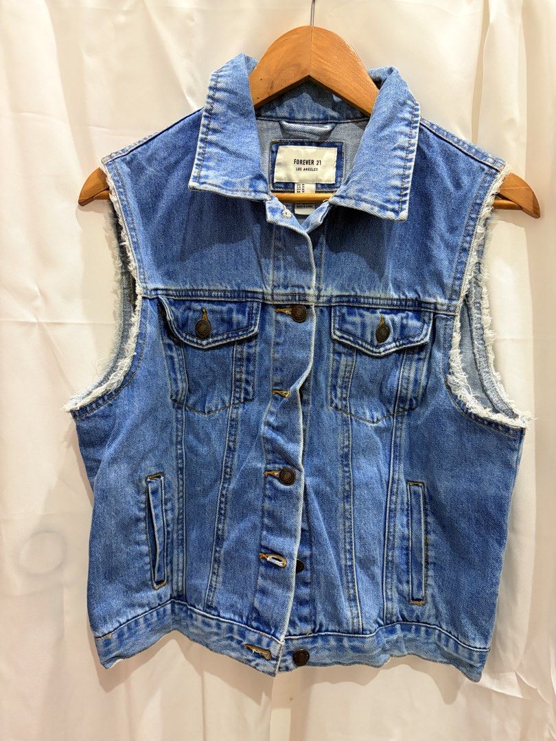 Forever 21 Blue Denim Vest Raw Edge Size M (Category: Sleeveless) located in General Trias. Submitted by hayami.clo (Listing ID 1465386375, Image 1). Description: - Brand: Forever 21 - Size: Medium (tag attached) - Color: Medium wash blue - Design: Classic collar, button-down front with metal buttons - Details: Raw frayed armholes, chest flap pockets, and side welt pockets - Condition: Brand new with tags - Style: Great layering piece for casual 