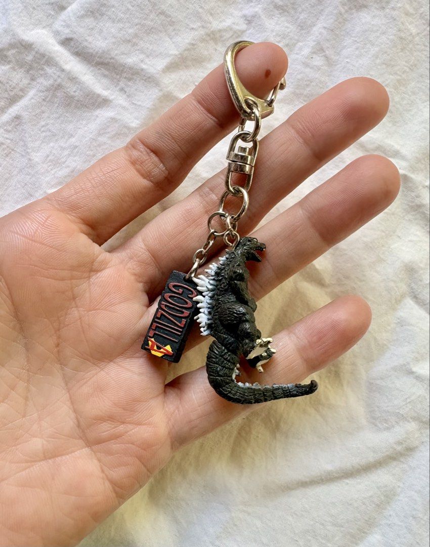 Godzilla Figurine Keychain with Logo Charm (Category: Character Goods) located in Tuguegarao City. Submitted by jasminecoll (Listing ID 1465535773, Image 2). Description: - Detailed Godzilla mini figure with textured scales and painted dorsal spines - Includes a matching logo charm - Sturdy metal keyring and secure clasp - Versatile accessory for keys, bags, or backpacks - Perfect gift or addition for Godzilla and monster fans -Location Tuguegara