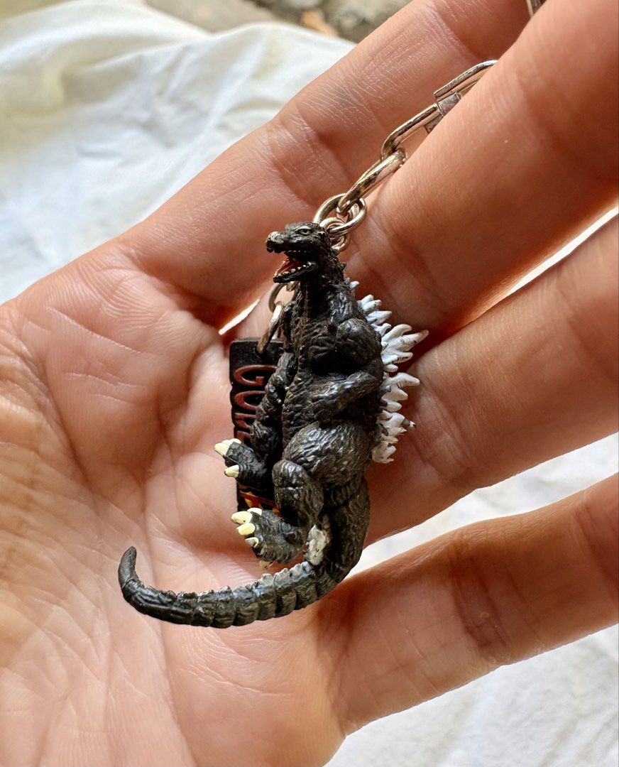 Godzilla Figurine Keychain with Logo Charm (Category: Character Goods) located in Tuguegarao City. Submitted by jasminecoll (Listing ID 1465535773, Image 3). Description: - Detailed Godzilla mini figure with textured scales and painted dorsal spines - Includes a matching logo charm - Sturdy metal keyring and secure clasp - Versatile accessory for keys, bags, or backpacks - Perfect gift or addition for Godzilla and monster fans -Location Tuguegara