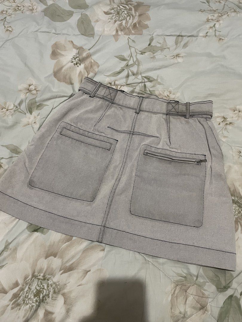 Grey Denim Mini Skirt with Cargo Pockets (Category: Skirts) located in Manila. Submitted by millewee12 (Listing ID 1465553788, Image 2). Description: - Color: Light grey denim with contrast black stitching - Fit: Mini skirt with built-in belt loops and front button/zip fly closure - Pockets: Front and back cargo-style pockets, plus an extra back zip pocket - Detail: Chic side zip at the hem - Style: Utility aesthetic, perfect for pairing with bas