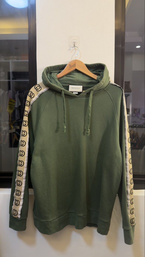 Gucci Interlocking G Olive Green Hoodie Size M (Category: Coats, Jackets and Outerwear) located in Paranaque City. Submitted by preluxeshop_ph (Listing ID 1465555586, Image 2). Description: Gucci Interlocking G Olive Green Hoodie Size M - Size: Medium (Made in Italy) - Cream and black jacquard stripe tape with interlocking G logo on both sleeves - Premium cotton loopback fleece fabric - Drawstring hood with ribbed cuffs and hem - Clean piece with