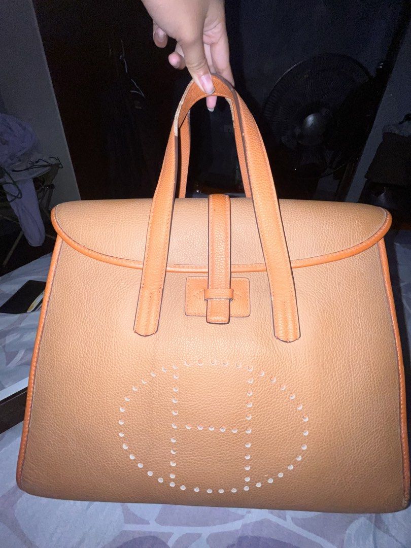Hermes Orange Leather Tote Handbag (Category: Shoulder Bags) located in Manila. Submitted by preloved_quality216 (Listing ID 1465560745, Image 2). Description: HEARING OFFERS! - Authentic Hermes leather tote bag in a stunning tan orange color - Structured, boxy silhouette with sturdy top handles and secure flap closure - Features the iconic perforated H logo punch-out design on the front - Impeccable, clean stitching along all trims and straps - 