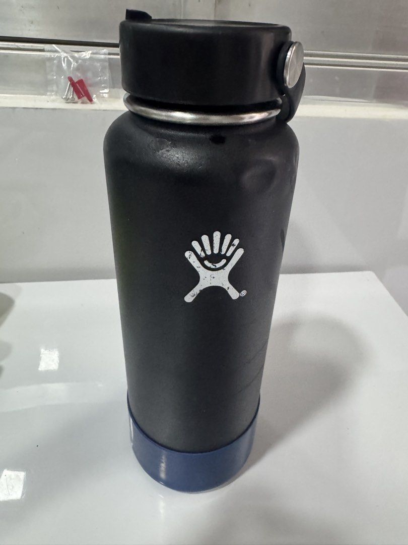Hydro Flask Water Bottle Black with Blue Boot (Category: Water Bottles & Tumblers) located in Manila. Submitted by decluterthings888 (Listing ID 1465396949, Image 2). Description: - Color: Black with blue silicone boot - Included: Standard black cap with handle - Branding: White Hydro Flask logo on the side - Condition: Normal signs of use, includes visible dents and scratches on the body and logo - 100% authentic and ready for daily use.