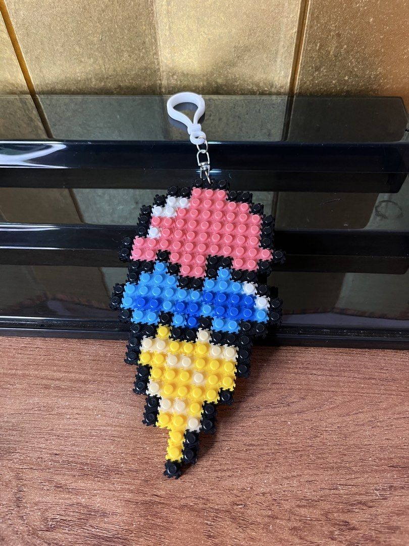 Ice cream cone pixel block keychain (Category: Character Goods) located in Gapan. Submitted by lunashop14 (Listing ID 1465565025, Image 1). Description: - Handmade ice cream cone keychain made from mini pixel blocks - Features pink and blue scoops with black outlines and a yellow waffle cone - Equipped with a white plastic clasp ring for easy hanging - Fun and colorful accessory perfect for bags, keys, or lanyards - Lightweight, unique, and great