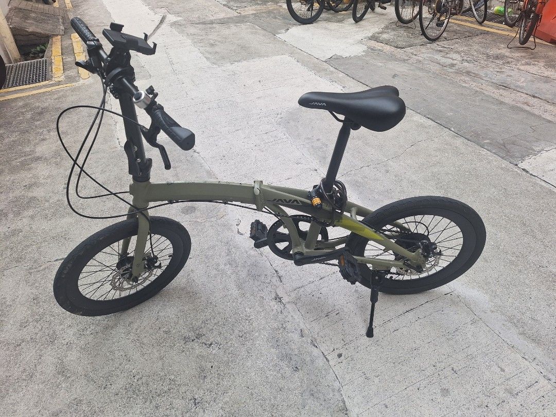 JAVA Green Folding Bicycle (Category: Bicycles) located in Singapore. Submitted by mdmonirujj67123 (Listing ID 1465439760, Image 6). Description: - Brand: JAVA - Color: Green with black saddle, handlebars, and wheels - Brakes: Reliable disc brakes - Portability: Lightweight and folds smoothly for storage or public transport - Included Accessories: Mounted kickstand, phone holder, bell, and coiled combination lock - Ideal For: Urban commuting and 