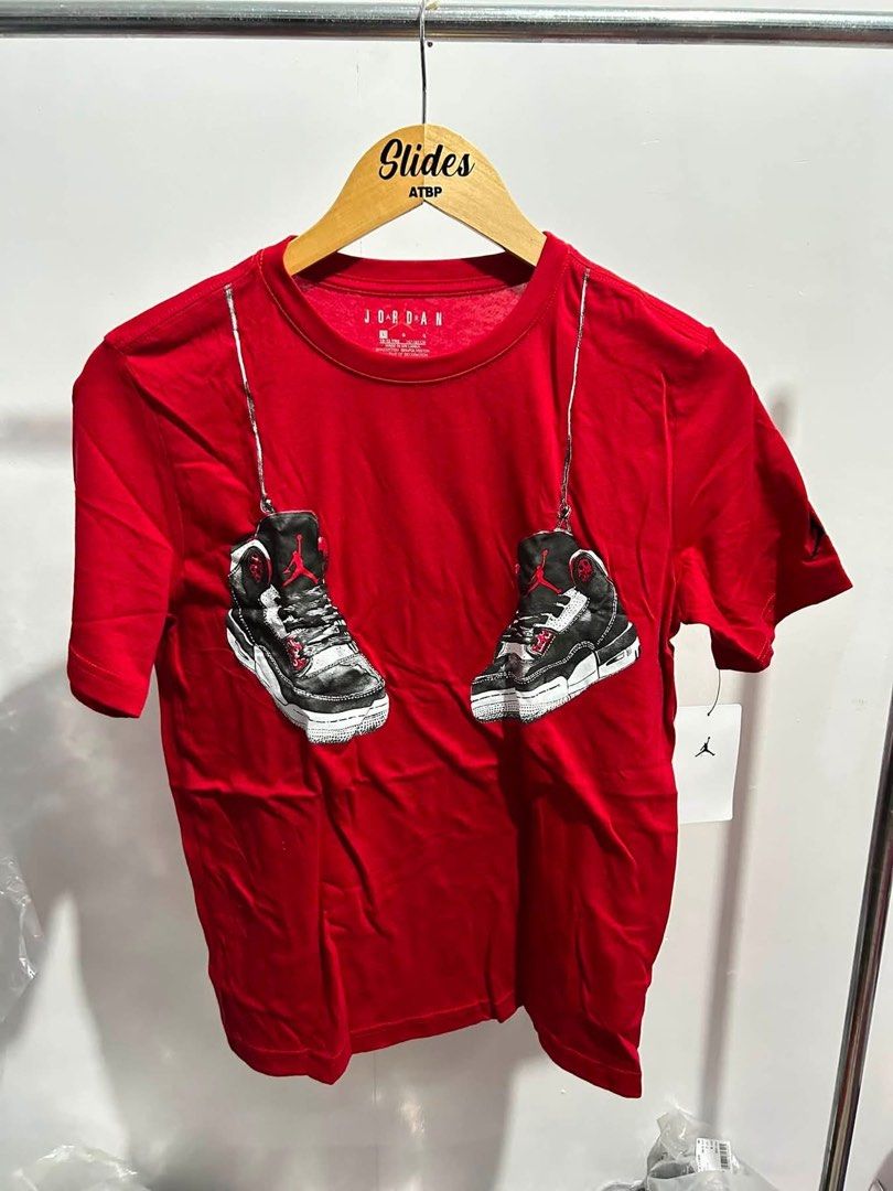 Jordan Red Graphic T-Shirt (Category: Tshirts & Polo Shirts ) located in Agdangan. Submitted by chano11339 (Listing ID 1465559902, Image 1). Description: - Brand: Jordan - Color: Bright red - Design: Graphic print of sneakers hanging down the front - Details: Crew neck, short sleeves - Condition: Brand new with original tag attached to the side seam, graphic has no cracks or fading.