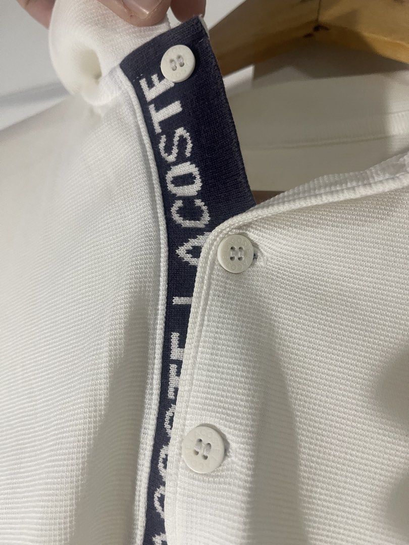 Lacoste White Polo Shirt with Contrast Placket (Category: Tshirts & Polo Shirts ) located in Manila. Submitted by kyllyzzle (Listing ID 1465562403, Image 3). Description: White short sleeve polo shirt from Lacoste. Textured pique fabric throughout. Navy blue placket interior featuring bold white LACOSTE lettering down the button closure. Two white branded buttons at the neck. Classic collar style. Clean back with no graphics. Simple casual piece 