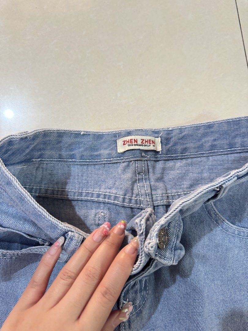 Light wash blue Denim Skirt (Category: Skirts) located in Quezon City. Submitted by sweetlyluxe (Listing ID 1465481986, Image 2). Description: - Brand: Zhen Zhen - Size: fit small - Wash: Light wash denim - Style: High-waist with classic belt loops, front zip fly, and button closure - Details: Functional front and back pockets with a stylish raw hem finish - Versatility: Perfect for pairing with casual tees and crop tops.