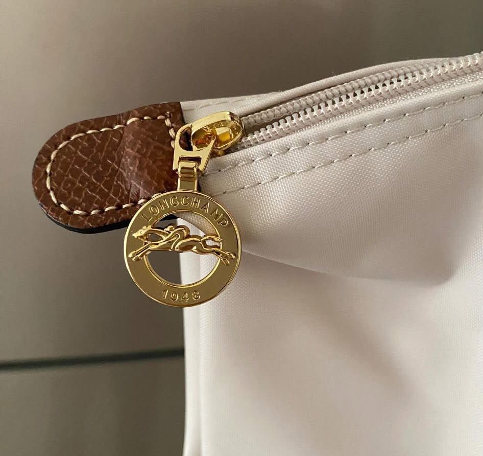 Longchamp Le Pliage Paper (Category: Luxury Bags & Wallets) located in Paoay. Submitted by rvf1230 (Listing ID 1465390114, Image 3). Description: - Color & Material: Paper color nylon body with brown leather handles and flap - Hardware: Gold tone zipper pull with horse logo and 1948 stamp, plus front flap snap button closure - Interior: Clean white lining with convenient slip pockets - Straps: Double shoulder straps with stylish contrast stitchin