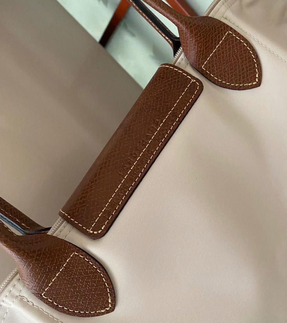 Longchamp Le Pliage Paper (Category: Luxury Bags & Wallets) located in Paoay. Submitted by rvf1230 (Listing ID 1465390114, Image 2). Description: - Color & Material: Paper color nylon body with brown leather handles and flap - Hardware: Gold tone zipper pull with horse logo and 1948 stamp, plus front flap snap button closure - Interior: Clean white lining with convenient slip pockets - Straps: Double shoulder straps with stylish contrast stitchin