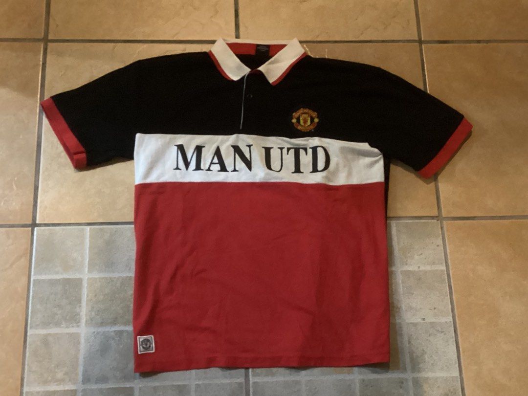 Manchester United Polo (Category: Tshirts & Polo Shirts ) located in Manila. Submitted by jellythrift.ph (Listing ID 1465484836, Image 2). Description: - Authentic Manchester United official merchandise - Size: Large (L) - Color block design in black, white, and red - Bold 'MAN UTD' chest print and embroidered team crest - Features a collar with button closure and small woven hem badge - Crafted from comfortable and breathable pique cotton.