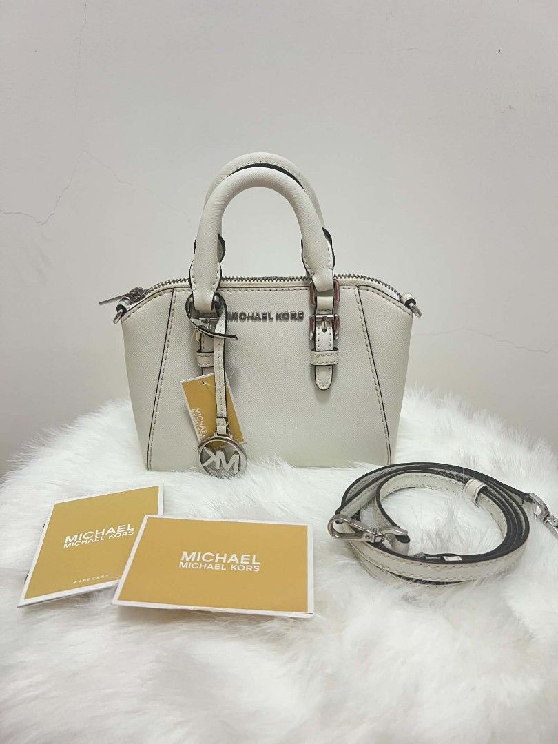 Michael Kors Mini Ciara Crossbody Bag (Category: Cross-body Bags) located in Paoay. Submitted by rvf1230 (Listing ID 1465423908, Image 1). Description: - Authentic Michael Kors dome satchel in crisp white Saffiano leather - Silver-tone hardware with front MK lettering and logo charm hangtag - Dual top handles and adjustable, removable crossbody strap - Top zip closure with clean MK signature interior lining - Includes interior slip pockets and ca