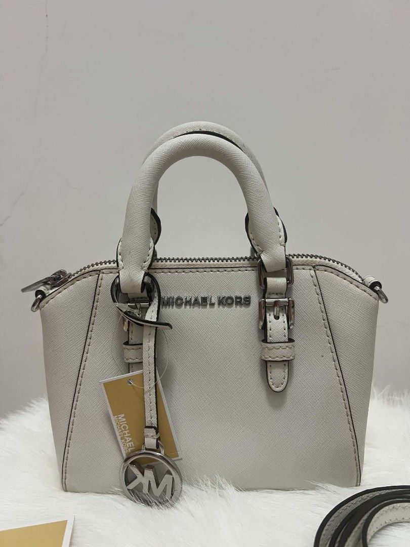 Michael Kors Mini Ciara Crossbody Bag (Category: Cross-body Bags) located in Paoay. Submitted by rvf1230 (Listing ID 1465423908, Image 2). Description: - Authentic Michael Kors dome satchel in crisp white Saffiano leather - Silver-tone hardware with front MK lettering and logo charm hangtag - Dual top handles and adjustable, removable crossbody strap - Top zip closure with clean MK signature interior lining - Includes interior slip pockets and ca