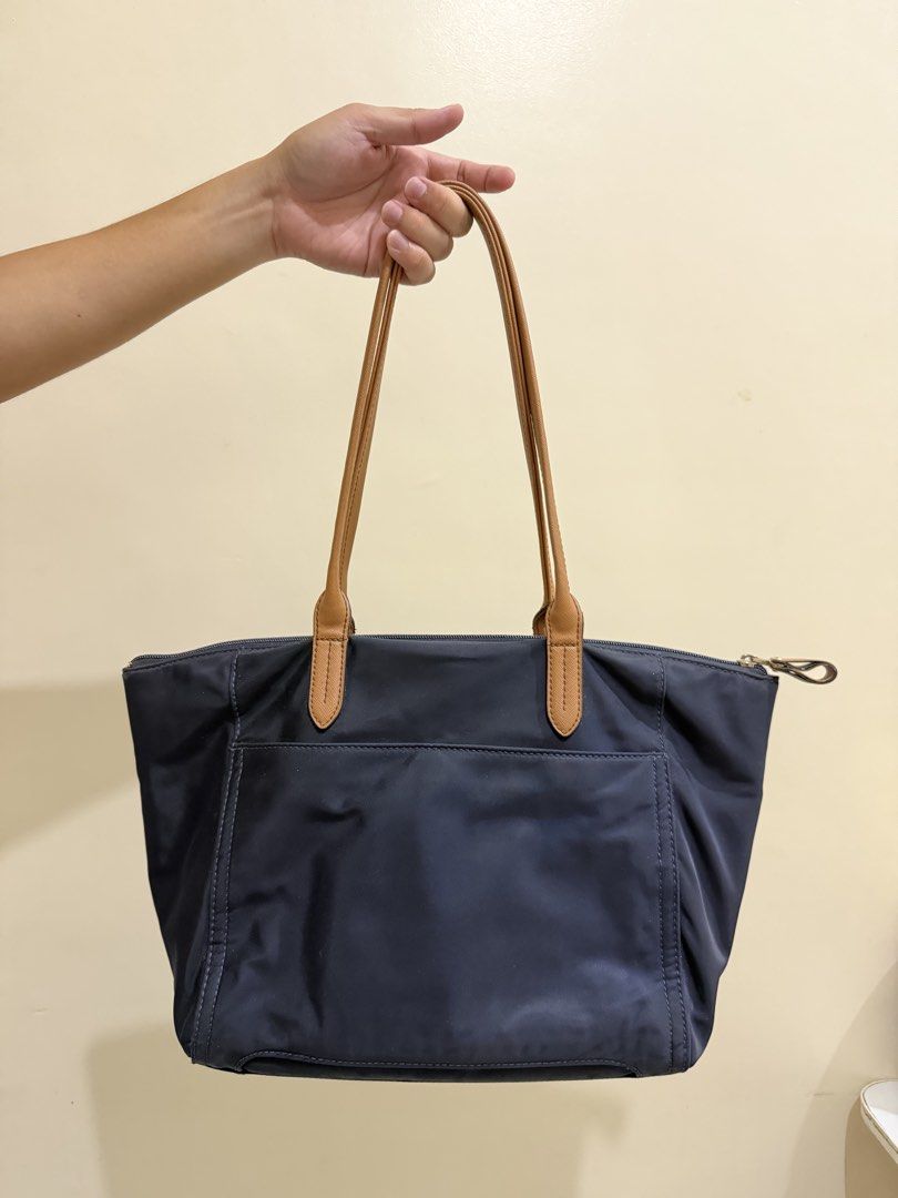 Michael Kors Navy Blue Nylon Tote Bag (Category: Tote Bags) located in San Pedro. Submitted by napnap29 (Listing ID 1465497571, Image 2). Description: - Brand: Michael Kors - Color: Navy blue with tan leather straps and trim - Hardware: Gold-tone - Exterior: Front zipper pocket with logo plaque, back slip pocket - Closure: Top zipper closure - Interior: Dark fabric lining with multiple slip pockets and one zippered pocket - Capacity: Spacious eve
