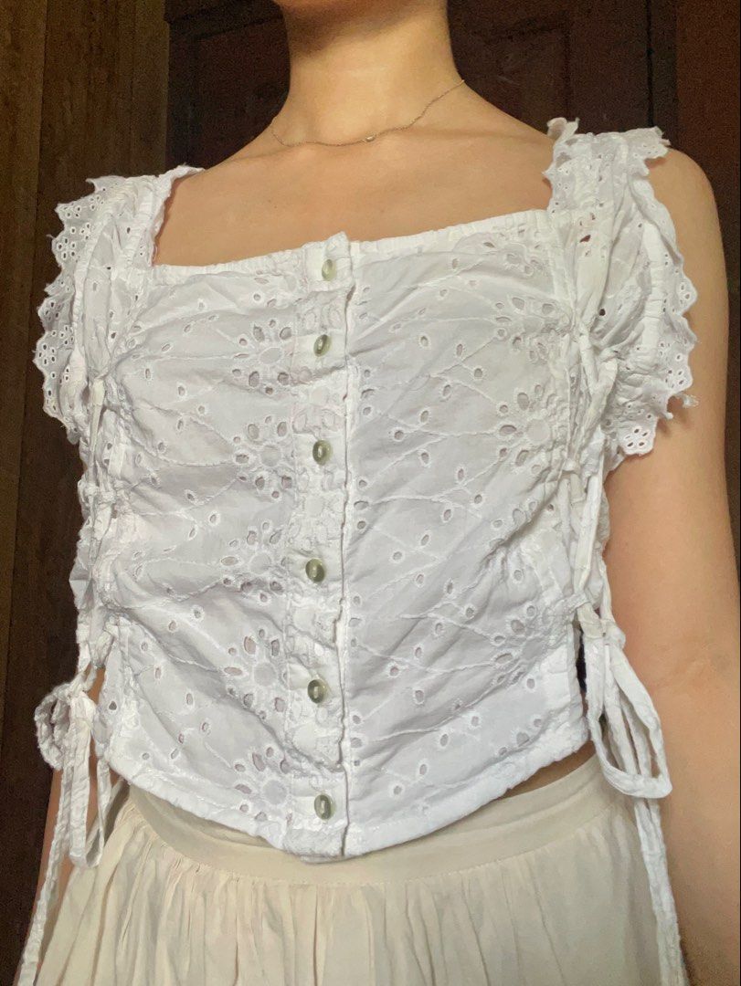 Nasty Gal White Eyelet Crop Top (Category: Sleeveless) located in Antipolo. Submitted by jazzminex (Listing ID 1465534692, Image 1). Description: - Brand: Nasty Gal - Style: Cottagecore white eyelet crop top - Details: Square neckline, front buttons, side tie details, low open back - Straps: Ruffled trim - Fabric: Lightweight and breathable - Condition: Excellent.
