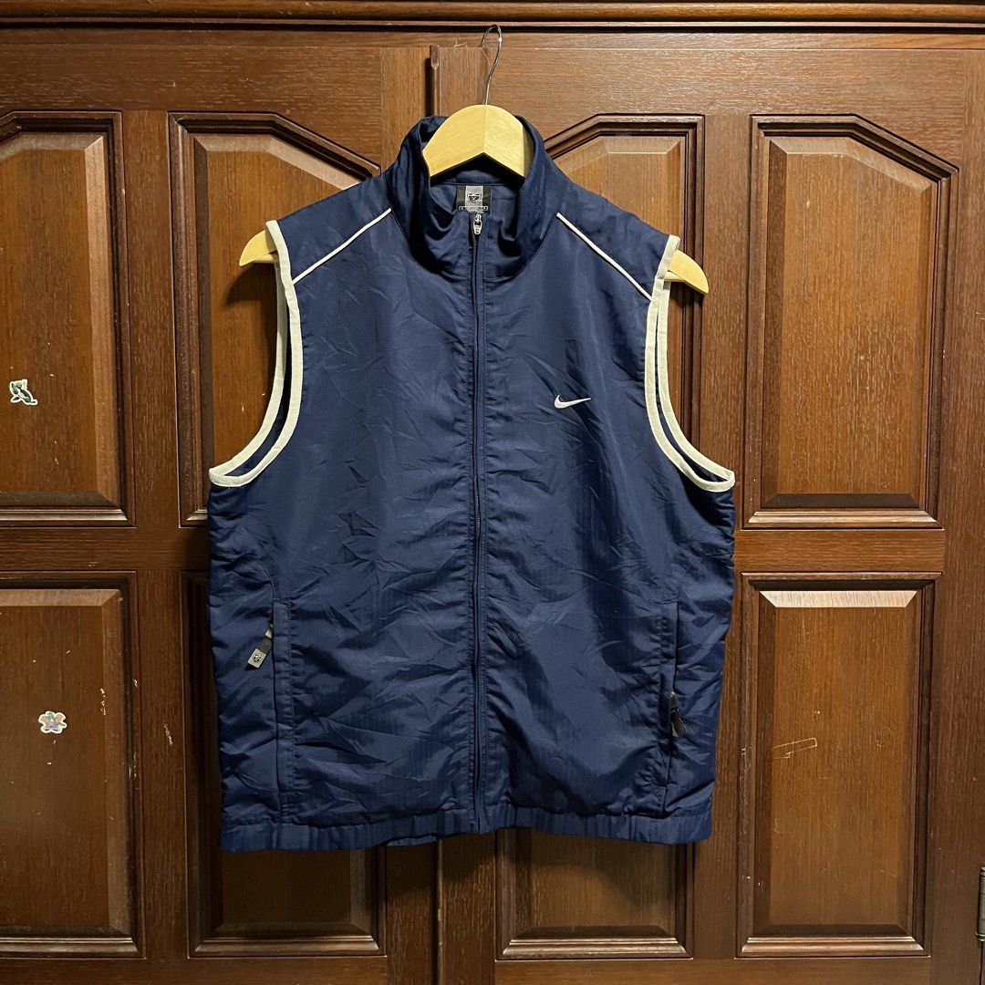 Nike Golf Navy Blue Zip-Up Vest (Category: Vests) located in Manila. Submitted by thriftyyyyy. (Listing ID 1465533485, Image 1). Description: - Brand: Nike Golf - Color: Navy blue with white piping trim - Material: Lightweight fabric with grid texture - Design: Full zip front, high collar, two zippered hand pockets - Details: Embroidered Nike swoosh on chest and Nike Golf logo patch on back collar - Condition: Excellent/Ready to wear.