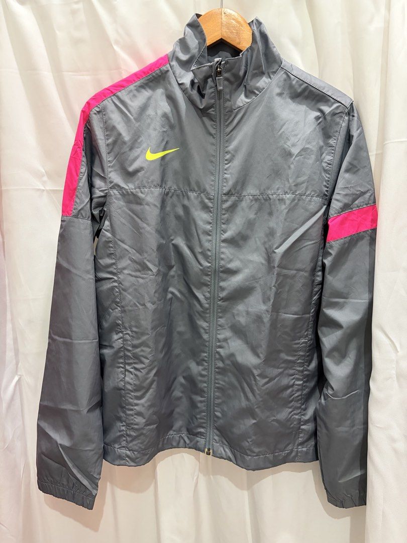 Nike Gray and Pink Windbreaker Jacket Size S (Category: Coats, Jackets and Outerwear) located in General Trias. Submitted by hayami.clo (Listing ID 1465386309, Image 1). Description: Gray Nike windbreaker with bright pink shoulder stripes and neon yellow swoosh logo on the chest. Full zip front with stand-up collar. Two zippered side pockets for secure storage. Lightweight mesh lining inside. Size S, made in Indonesia. 100% polyester material. Cl