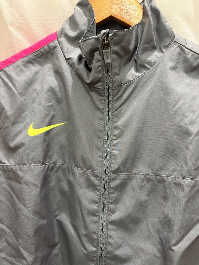 Nike Gray and Pink Windbreaker Jacket Size S (Category: Coats, Jackets and Outerwear) located in General Trias. Submitted by hayami.clo (Listing ID 1465386309, Image 2). Description: Gray Nike windbreaker with bright pink shoulder stripes and neon yellow swoosh logo on the chest. Full zip front with stand-up collar. Two zippered side pockets for secure storage. Lightweight mesh lining inside. Size S, made in Indonesia. 100% polyester material. Cl