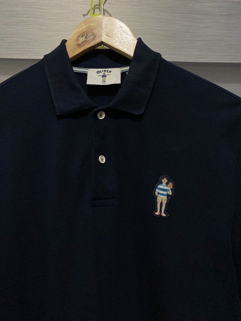 OLIVER Navy Polo Shirt with Character Patch (Category: Tshirts & Polo Shirts ) located in Butuan. Submitted by nielben13 (Listing ID 1465498925, Image 2). Description: - Brand: OLIVER - Color: Navy Blue - Size: 100 - Style: Short sleeves, button collar, and side slits at the hem - Detail: Embroidered character patch on the left chest - Condition: Clean, well-maintained, with minimal signs of wear.