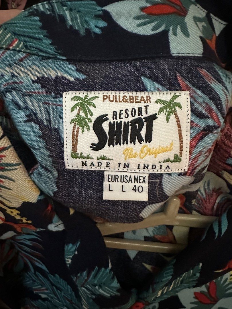 Pull&Bear Tropical Floral Resort Shirt Size L (Category: Shirts) located in Marikina City. Submitted by blk1012_ (Listing ID 1465569042, Image 3). Description: - Brand: Pull&Bear - Style: Tropical resort shirt / Camp collar - Color: Dark navy blue with vibrant floral and palm tree print - Size: EUR/USA L (MEX 40) - fits true to size - Material/Origin: Made in India - Condition: Great casual piece for summer or beach trips.