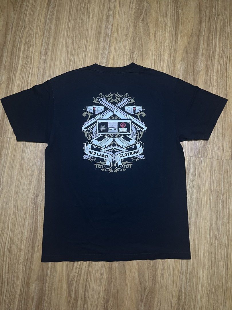 Red Label Clothing Large •21x29 (Category: Tshirts & Polo Shirts ) located in Cebu City. Submitted by guttathreads (Listing ID 1465429766, Image 3). Description: - Brand: Red Label Clothing - Color: Black - Style: Short sleeve crew neck t-shirt - Design: Retro NES controller graphic on chest; detailed crossed NES Zappers, consoles, and ornate scrollwork on the back - Condition: Excellent, no obvious flaws or fading - Size: Standard fit - Ideal fo