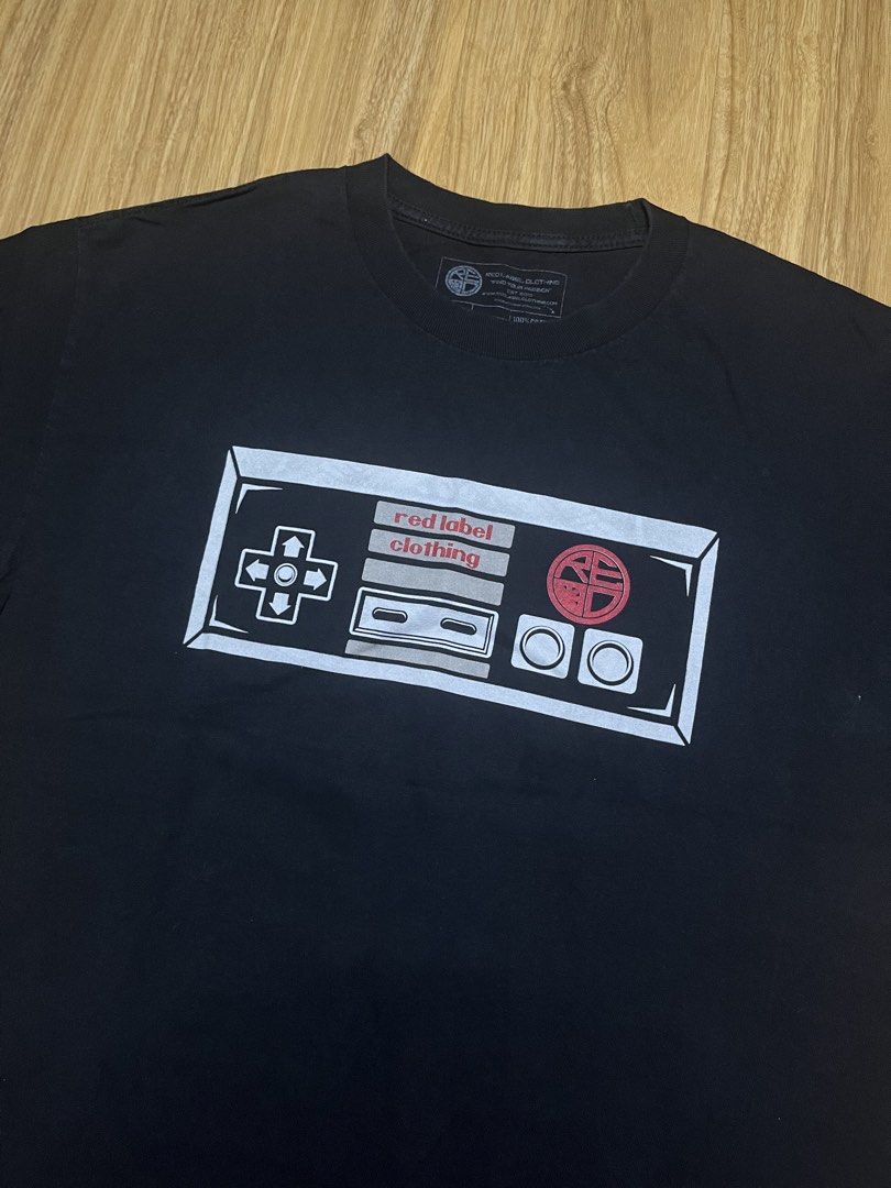 Red Label Clothing Large •21x29 (Category: Tshirts & Polo Shirts ) located in Cebu City. Submitted by guttathreads (Listing ID 1465429766, Image 2). Description: - Brand: Red Label Clothing - Color: Black - Style: Short sleeve crew neck t-shirt - Design: Retro NES controller graphic on chest; detailed crossed NES Zappers, consoles, and ornate scrollwork on the back - Condition: Excellent, no obvious flaws or fading - Size: Standard fit - Ideal fo