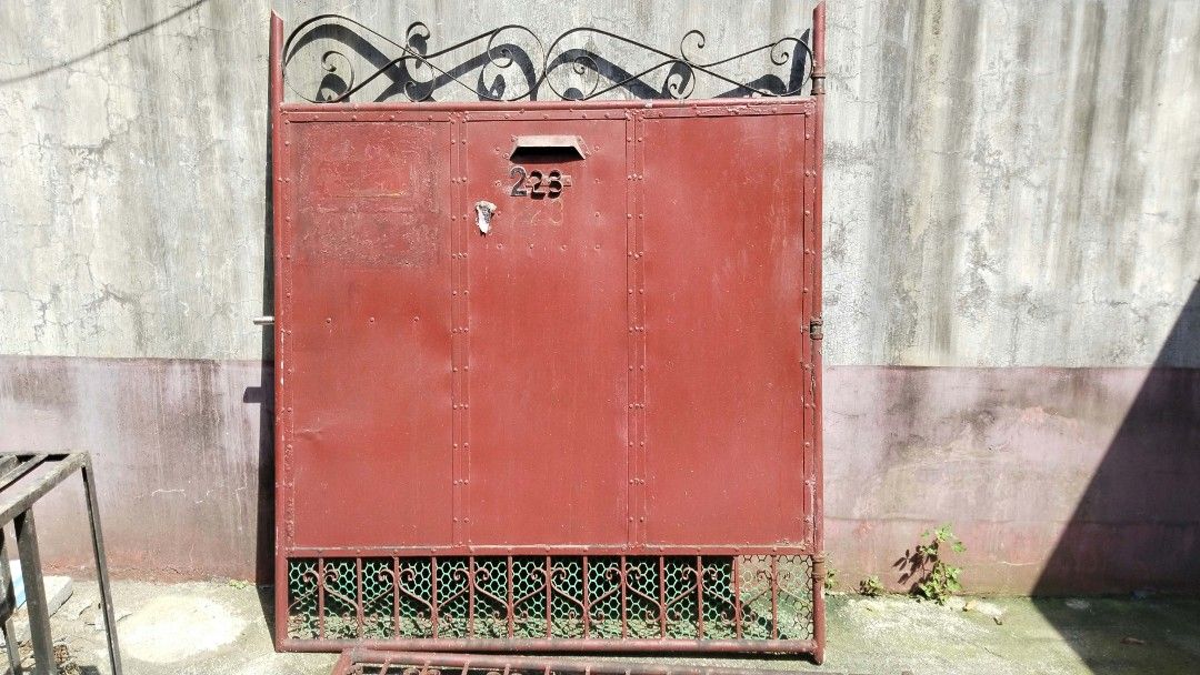 Red metal driveway gate with decorative scrollwork and mailbox (Category: Locks, Doors & Gates) located in Manila. Submitted by bravecloud-dcbf6c (Listing ID 1465409318, Image 2). Description: - Color & Design: Solid red metal with decorative black scrollwork at the top and mesh grating at the bottom - Features: Includes a built-in mailbox slot and latch hardware - Condition: Sturdy and heavy-duty, with visible weathering, scuffs, and paint wear 