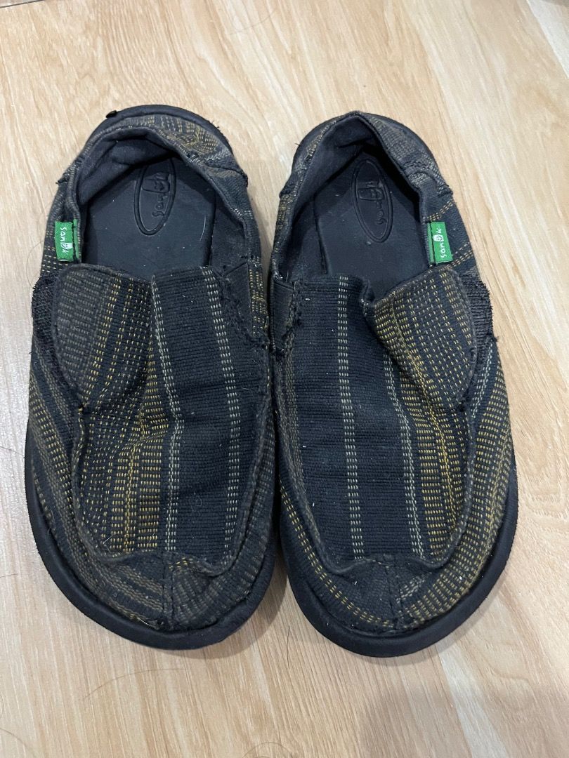 Sanuk Slip-On Shoes Black Patterned (Category: Babies & Kids Fashion) located in Pasig City. Submitted by chepshoppe (Listing ID 1465388390, Image 1). Description: - Brand: Sanuk - size Cm:20; Eur: 32 - Style: Casual slip-on shoes - Color/Design: Black and yellow patterned fabric with green logo tags - Features: Flexible soles and soft black footbeds - Condition: Normal wear from use, perfect for everyday walking or relaxing.