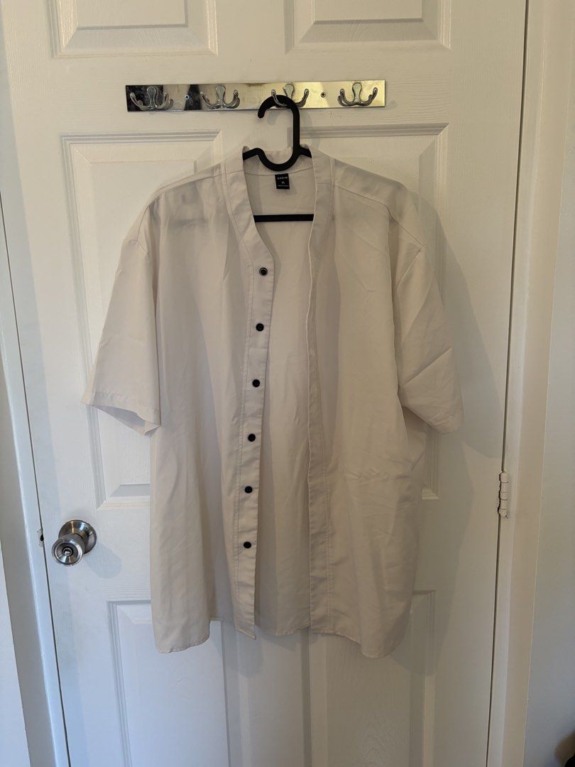 SHEIN White Button-Up Short Sleeve Shirt (Category: Tshirts & Polo Shirts ) located in Marikina City. Submitted by pong15 (Listing ID 1465500942, Image 1). Description: - Brand: SHEIN - Size: XL - Color: White with contrasting black buttons - Fit: Relaxed fit - Neckline: Collarless V-neck - Style: Short sleeve button-up - Condition: Great casual basic for everyday wear.