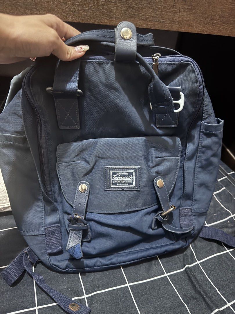 Technopack Navy Blue Backpack with Front Pocket (Category: Backpacks) located in Pasig City. Submitted by oinkrowie (Listing ID 1465497012, Image 1). Description: - Color: Dark Navy Blue - Features: Front pouch pocket with buckled straps, woven brand patch, dual top carry handles, and adjustable shoulder straps - Storage: Wide-opening zippered main compartment with interior mesh pockets and organizers - Condition: Minor fabric wear from normal us