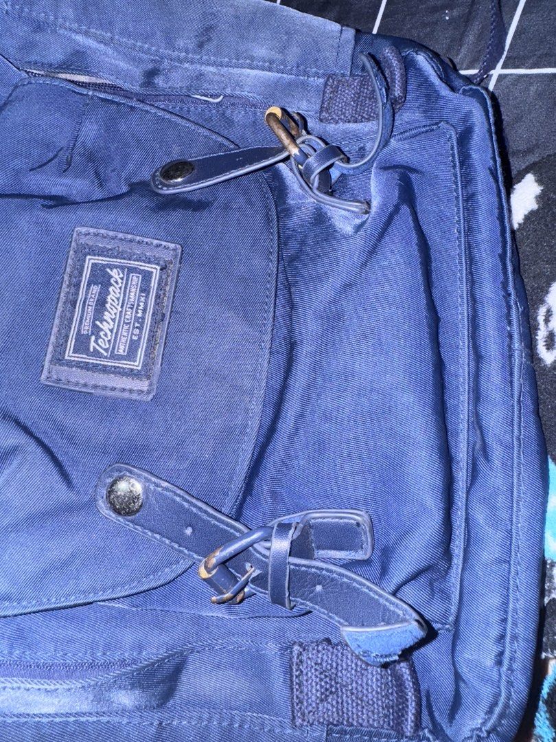 Technopack Navy Blue Backpack with Front Pocket (Category: Backpacks) located in Pasig City. Submitted by oinkrowie (Listing ID 1465497012, Image 3). Description: - Color: Dark Navy Blue - Features: Front pouch pocket with buckled straps, woven brand patch, dual top carry handles, and adjustable shoulder straps - Storage: Wide-opening zippered main compartment with interior mesh pockets and organizers - Condition: Minor fabric wear from normal us