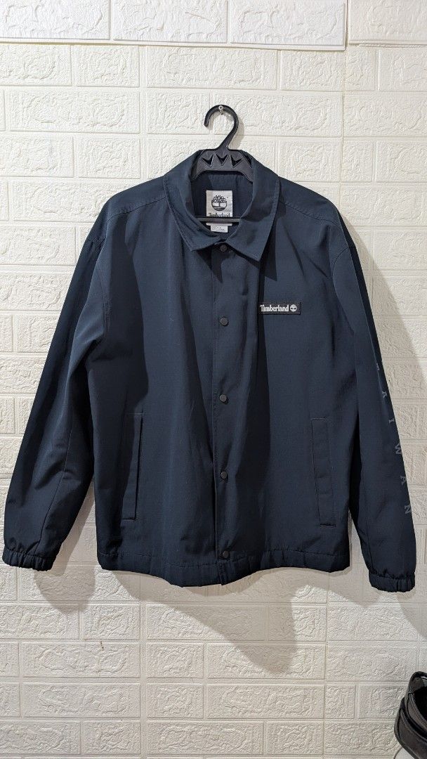 Timberland Navy Blue Coach Jacket (Category: Coats, Jackets and Outerwear) located in Angeles City. Submitted by quiroz028 (Listing ID 1465555721, Image 1). Description: - Brand: Timberland - Style: Coach jacket - Color: Navy blue - Size: Medium 24Wx 26 1/2L inches laid flat - Features: Front button closure, two side pockets, and elastic cuffs - Details: Large Timberland tree logo on the back - Interior: Gold 'TIMBS ON MY FEET' text lining negoti