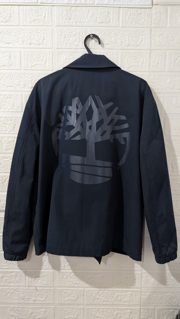 Timberland Navy Blue Coach Jacket (Category: Coats, Jackets and Outerwear) located in Angeles City. Submitted by quiroz028 (Listing ID 1465555721, Image 2). Description: - Brand: Timberland - Style: Coach jacket - Color: Navy blue - Size: Medium 24Wx 26 1/2L inches laid flat - Features: Front button closure, two side pockets, and elastic cuffs - Details: Large Timberland tree logo on the back - Interior: Gold 'TIMBS ON MY FEET' text lining negoti