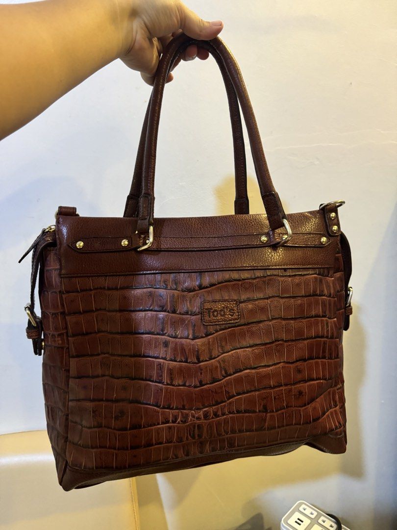 Tod's Brown Crocodile Embossed Leather Tote Bag (Category: Tote Bags) located in Urdaneta. Submitted by kathleenja24136 (Listing ID 1465472019, Image 1). Description: - Authentic Tod's leather handbag in a rich brown shade - Striking crocodile-embossed texture on the lower half - Comfortable dual shoulder straps and elegant gold-tone hardware - Signature debossed Tod's logo patch on the front - Secure zip closure with adjustable buckle strap side