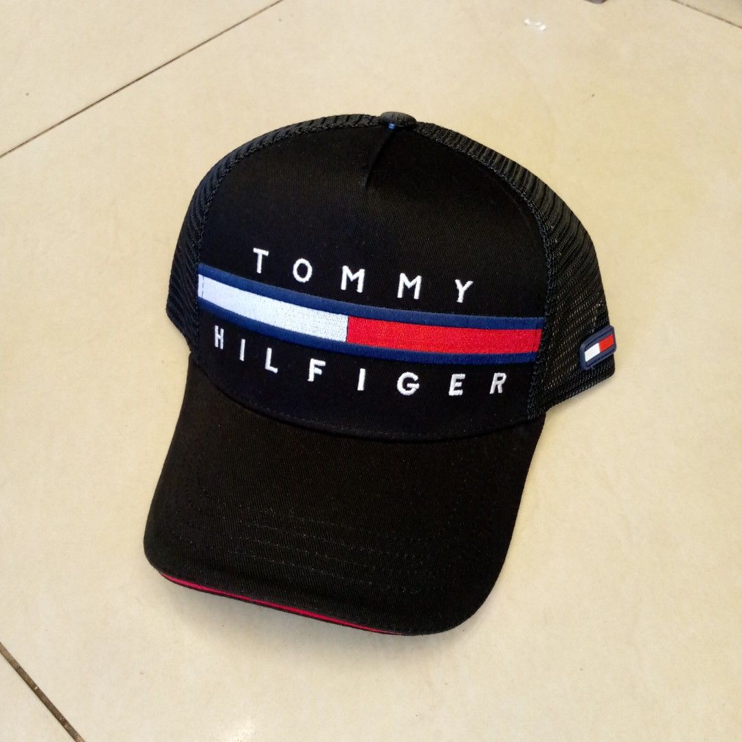 Tommy Hilfiger Black Trucker Cap (Category: Caps & Hats) located in Manila. Submitted by pablopresk0. (Listing ID 1465504026, Image 1). Description: Black Tommy Hilfiger trucker cap with mesh back panels. Classic embroidered logo across the front in white, red, and blue. Includes interior branded taping and adjustable snapback closure. Red piping along the brim edge and a small rubber logo flag on the side. Tags still attached. Manila location📍 