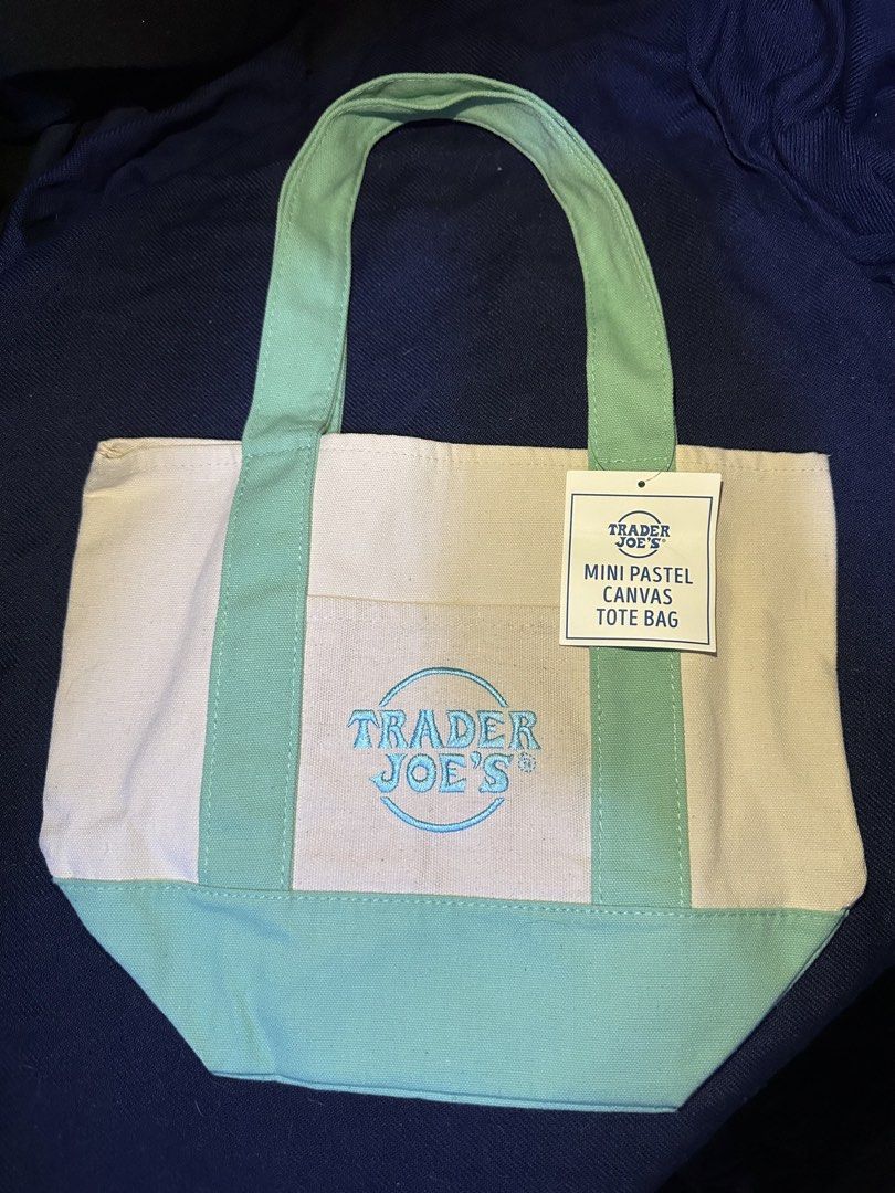 Trader Joe's Mini Pastel Canvas Tote Bag (Category: Tote Bags) located in Mandaluyong City. Submitted by nanokimber71869 (Listing ID 1465560710, Image 1). Description: - Brand new with tag attached - Color: Mint green and white pastel canvas - Material: Durable heavyweight canvas construction - Design: Front pocket featuring a blue embroidered Trader Joe's logo - Features: Double top handles and a structured base for easy storage - Condition: Pri