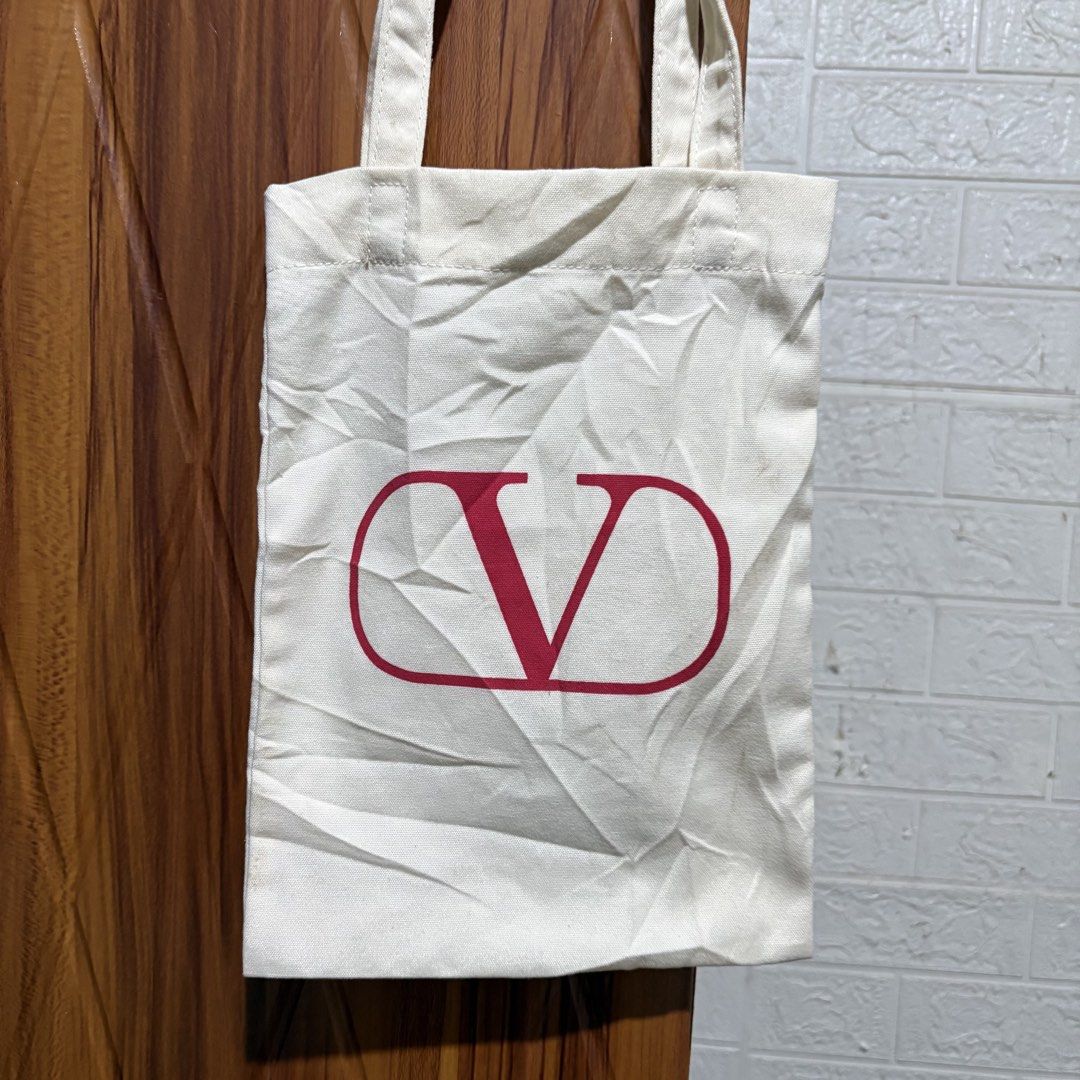 Valentino Canvas Tote Bag White Red Logo (Category: Tote Bags) located in Carmen. Submitted by rr_thrifts (Listing ID 1465400970, Image 2). Description: - Brand: Valentino - Color: Off-white canvas with striking red front logo - Eco-friendly: Interior text indicates it is made from 100% recycled plastic (equivalent to four 1L bottles) - Details: Fabric label with Valentino logo sewn near the inner seam - Straps: Sturdy double shoulder straps for 