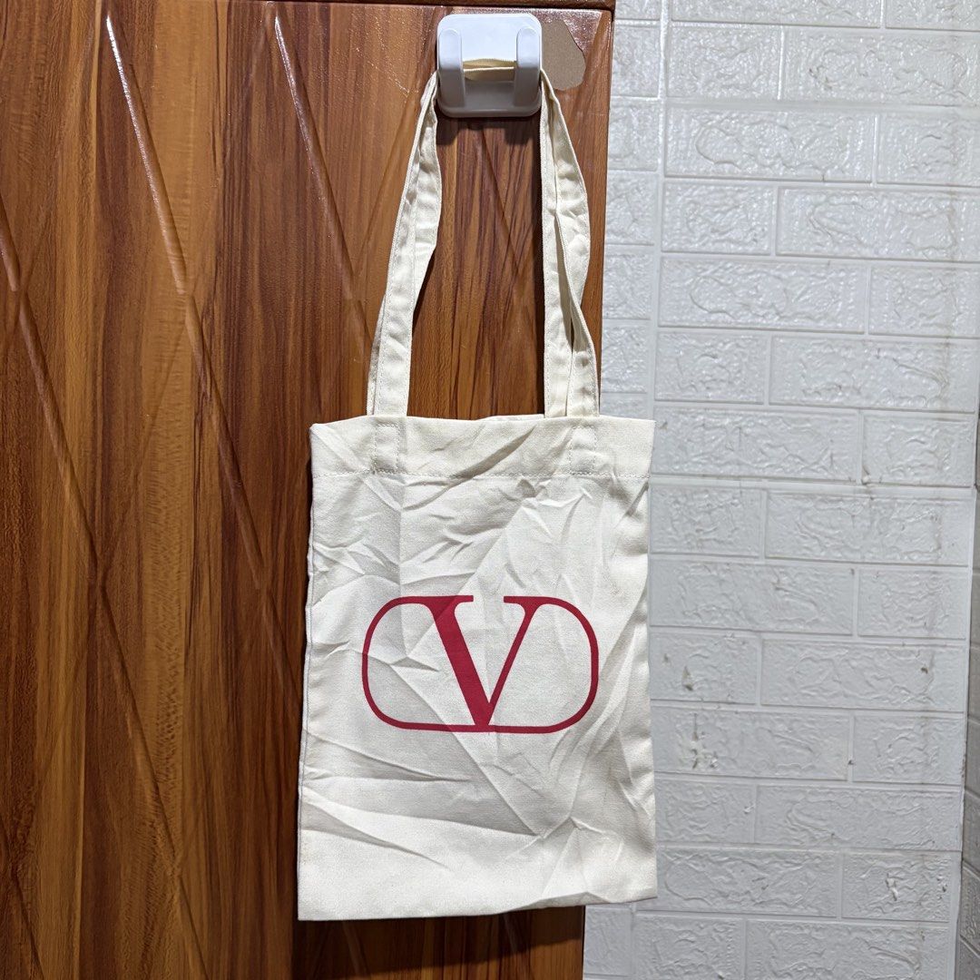 Valentino Canvas Tote Bag White Red Logo (Category: Tote Bags) located in Carmen. Submitted by rr_thrifts (Listing ID 1465400970, Image 1). Description: - Brand: Valentino - Color: Off-white canvas with striking red front logo - Eco-friendly: Interior text indicates it is made from 100% recycled plastic (equivalent to four 1L bottles) - Details: Fabric label with Valentino logo sewn near the inner seam - Straps: Sturdy double shoulder straps for 