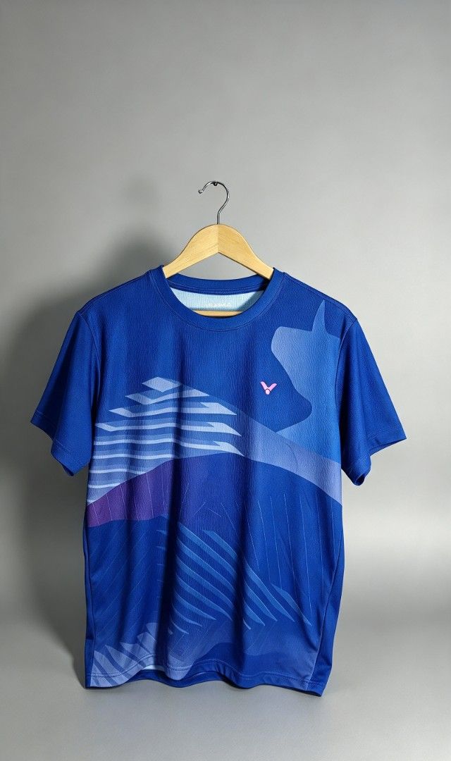Victor Badminton Jersey Blue (Category: Activewear) located in San Francisco. Submitted by Intaw20 (Listing ID 1465532969, Image 1). Description: - Brand: Victor - Color: Blue with abstract graphics and pink chest logo - Size: Asia XL (USA/EUR L) - Material: Lightweight, moisture-wicking polyester - Origin: Made in Taiwan - Condition: Clean, well-kept, and ready to wear - Ideal for: Badminton, gym workouts, and athletic training.