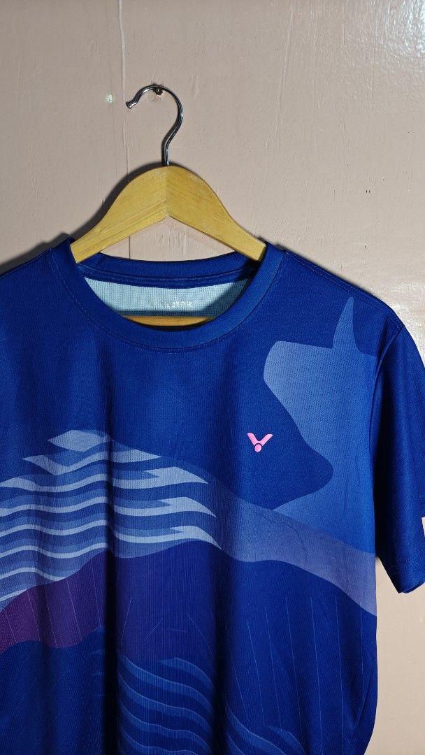 Victor Badminton Jersey Blue (Category: Activewear) located in San Francisco. Submitted by Intaw20 (Listing ID 1465532969, Image 2). Description: - Brand: Victor - Color: Blue with abstract graphics and pink chest logo - Size: Asia XL (USA/EUR L) - Material: Lightweight, moisture-wicking polyester - Origin: Made in Taiwan - Condition: Clean, well-kept, and ready to wear - Ideal for: Badminton, gym workouts, and athletic training.