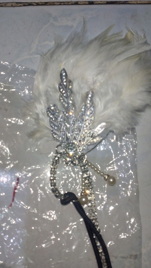 Vintage 1920s Flapper Feather Headband Rhinestone Headpiece (Category: Hair Accessories) located in Valenzuela. Submitted by diane.35 (Listing ID 1465501977, Image 2). Description: - Stunning white feather flapper headband for 1920s vintage vibes - Features a sparkling rhinestone leaf brooch with delicate rhinestone strands - Elegant dangling pearl beads for added movement and charm - Comfortable black elastic band fits most head sizes easily - I