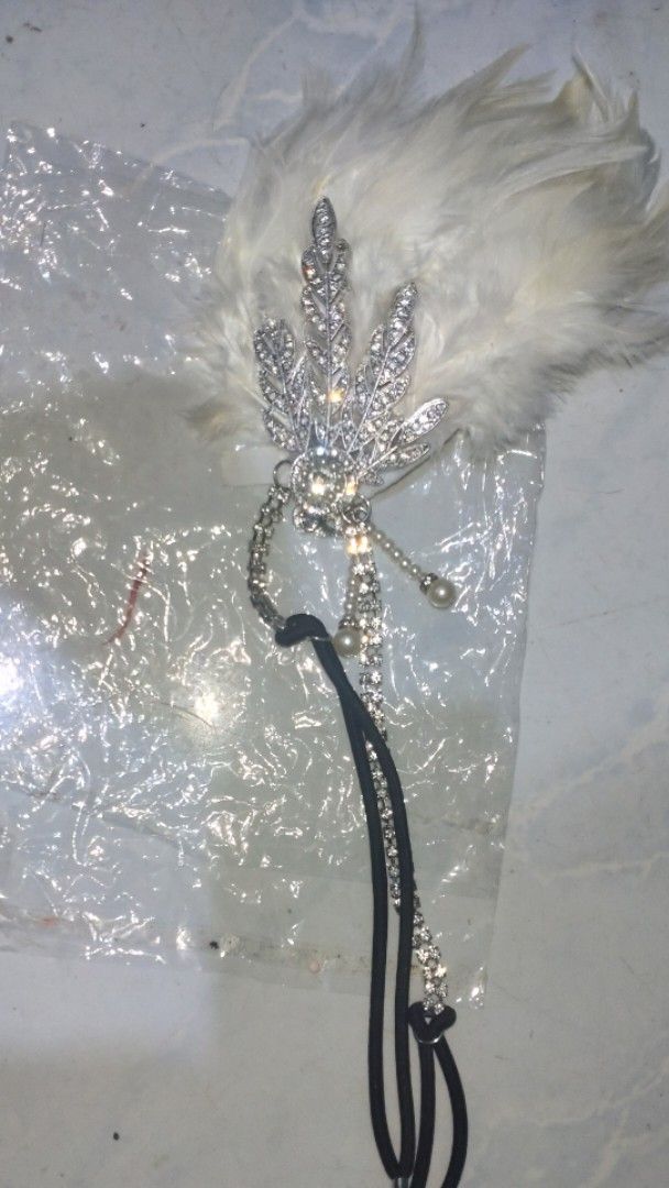 Vintage 1920s Flapper Feather Headband Rhinestone Headpiece (Category: Hair Accessories) located in Valenzuela. Submitted by diane.35 (Listing ID 1465501977, Image 1). Description: - Stunning white feather flapper headband for 1920s vintage vibes - Features a sparkling rhinestone leaf brooch with delicate rhinestone strands - Elegant dangling pearl beads for added movement and charm - Comfortable black elastic band fits most head sizes easily - I