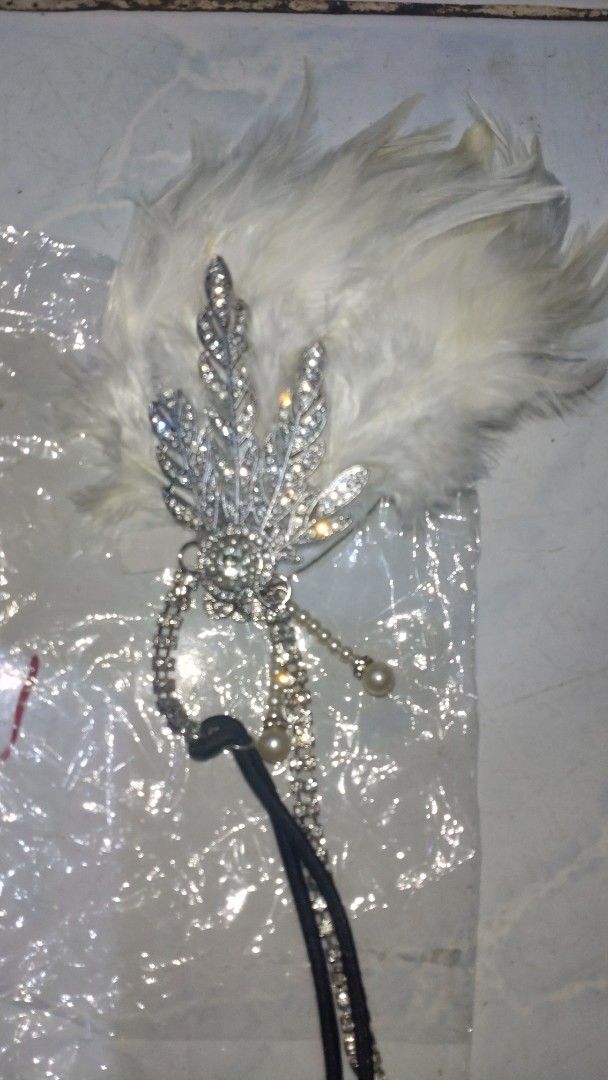 Vintage 1920s Flapper Feather Headband Rhinestone Headpiece (Category: Hair Accessories) located in Valenzuela. Submitted by diane.35 (Listing ID 1465501977, Image 3). Description: - Stunning white feather flapper headband for 1920s vintage vibes - Features a sparkling rhinestone leaf brooch with delicate rhinestone strands - Elegant dangling pearl beads for added movement and charm - Comfortable black elastic band fits most head sizes easily - I