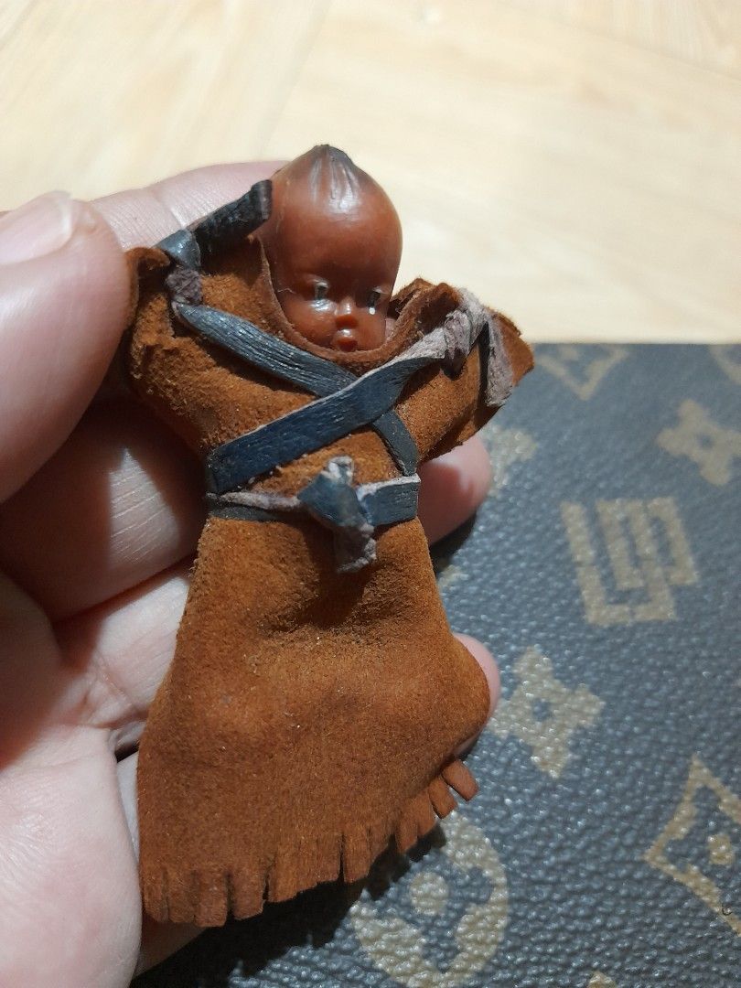 Vintage Mini Celluloid Native American Doll (Category: Vintage Collectibles) located in Bocaue. Submitted by marajapansurplus (Listing ID 1465428054, Image 3). Description: - Miniature swaddled baby doll figurine - Brown suede-like pouch with fringe trim - Detailed sculpted face and dark hair - Secured with black and tan leather straps - Palm-sized collectible item showcasing traditional craftsmanship.