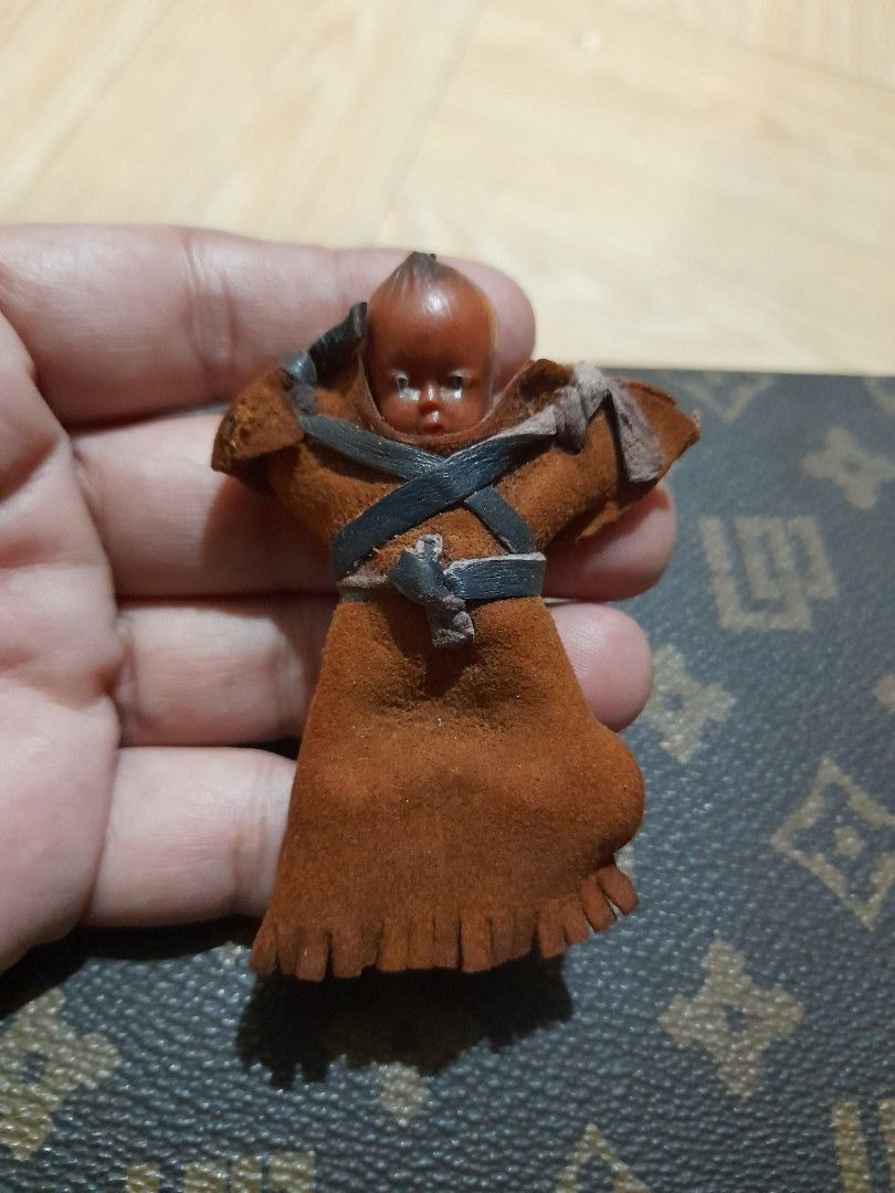 Vintage Mini Celluloid Native American Doll (Category: Vintage Collectibles) located in Bocaue. Submitted by marajapansurplus (Listing ID 1465428054, Image 1). Description: - Miniature swaddled baby doll figurine - Brown suede-like pouch with fringe trim - Detailed sculpted face and dark hair - Secured with black and tan leather straps - Palm-sized collectible item showcasing traditional craftsmanship.