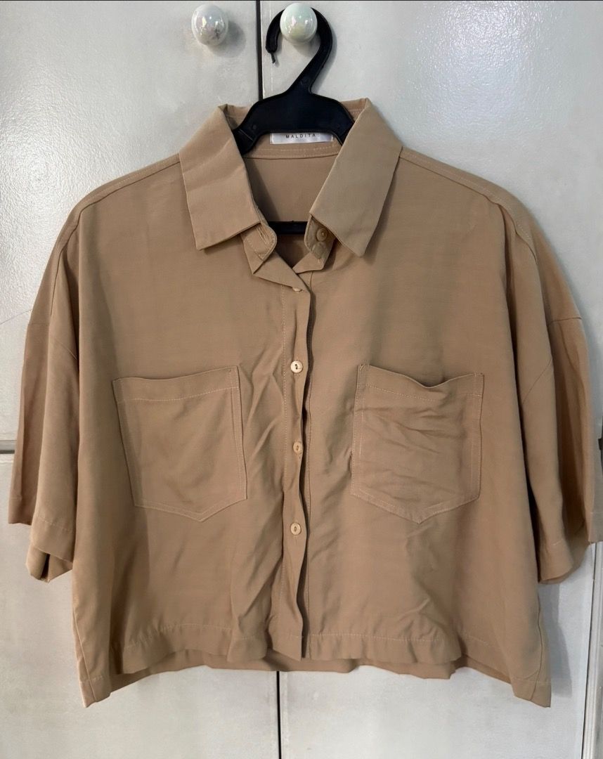 Cropped Button-Down Top (Category: Shirts) located in Santa Rosa. Submitted by biancamarie0404 (Listing ID 1465435160, Image 2). Description: - Brand: Maldita - Color: Classic beige - Style: Cropped button-down shirt with short sleeves - Details: Classic collar, light brown buttons, dual front chest pockets - Fit: Lightweight and flattering with high-waisted denim or trousers - Condition: Clean, excellent, and ready to wear.