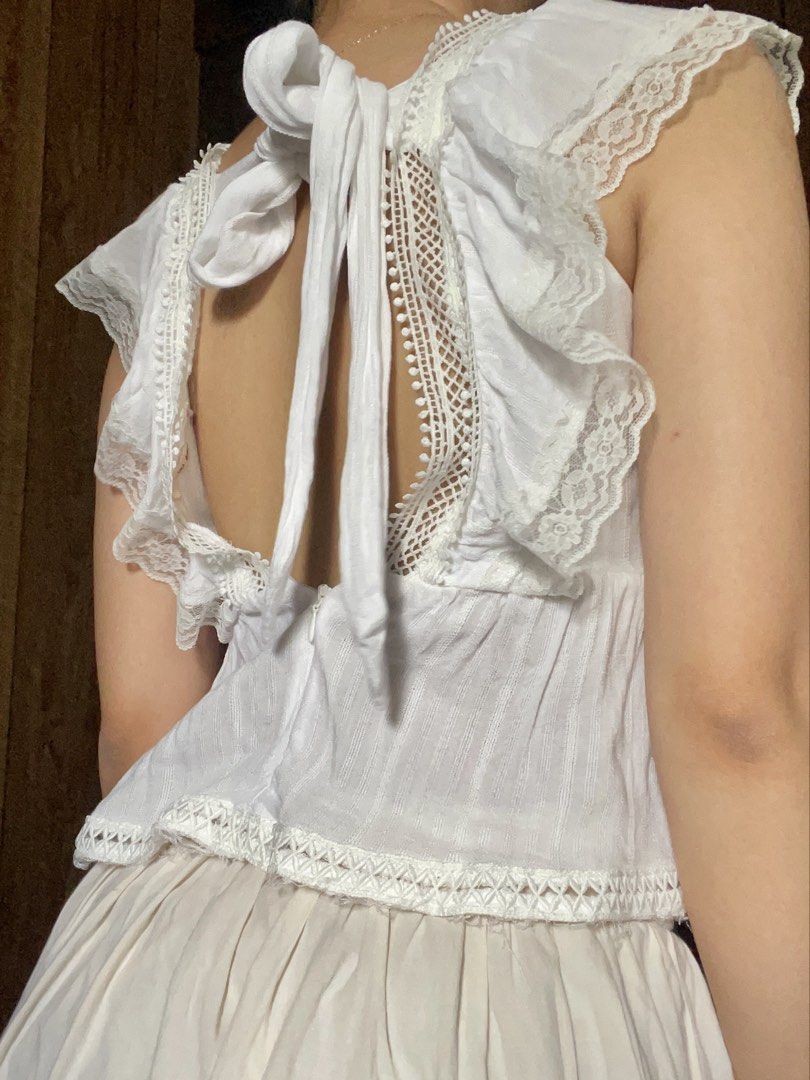 White lace trim ruffle tie-back crop top (Category: Sleeveless) located in Antipolo. Submitted by jazzminex (Listing ID 1465533467, Image 2). Description: - Style: Cottagecore sleeveless top - Design: Square neckline, low open back with fabric tie closure - Details: Ruffled lace shoulders, delicate crochet panels, and textured vertical stripes - Hem: Raw frayed edge hem with visible loose threads for a rustic look - Color: White.