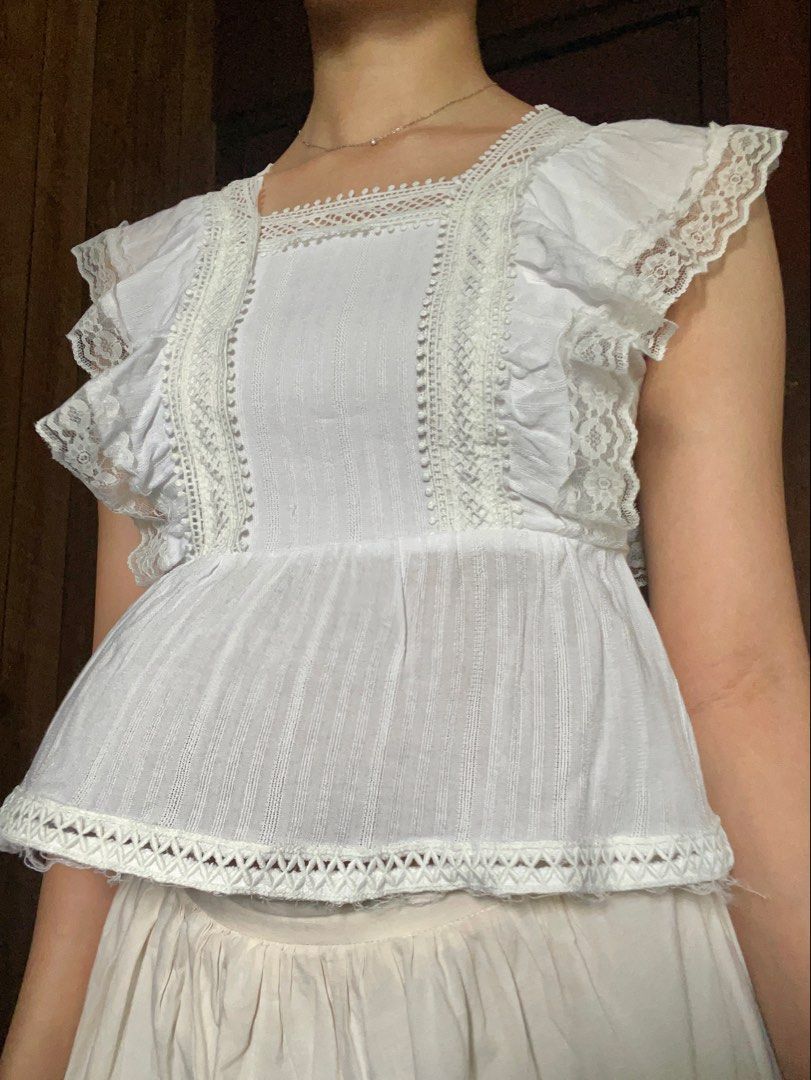 White lace trim ruffle tie-back crop top (Category: Sleeveless) located in Antipolo. Submitted by jazzminex (Listing ID 1465533467, Image 1). Description: - Style: Cottagecore sleeveless top - Design: Square neckline, low open back with fabric tie closure - Details: Ruffled lace shoulders, delicate crochet panels, and textured vertical stripes - Hem: Raw frayed edge hem with visible loose threads for a rustic look - Color: White.