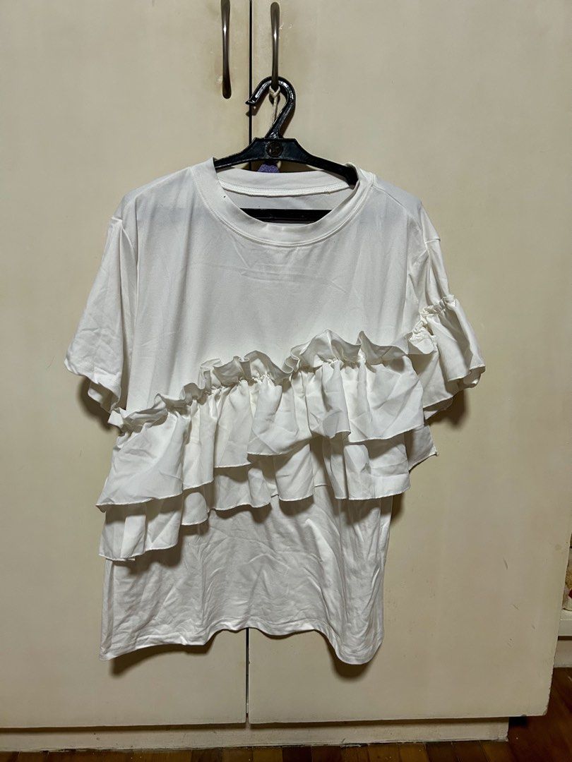 White T-shirt with Asymmetrical Ruffle Layer (Category: Shirts) located in Makati City. Submitted by monicavazquez (Listing ID 1465485714, Image 1). Description: - Color: White - Design: Diagonal layered ruffle front detail - Neckline: Crew neck - Fit: Relaxed and comfortable - Material: Soft cotton-blend fabric - Styling: Versatile; pairs easily with denim or skirts.